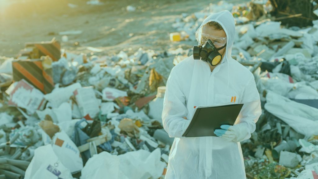 Man in full PPE in garbage dump using clipboard